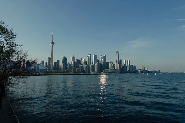 Toronto skyline with the CN Tower seen across Lake Ontario from a wooden boardwalk, on a bright day.